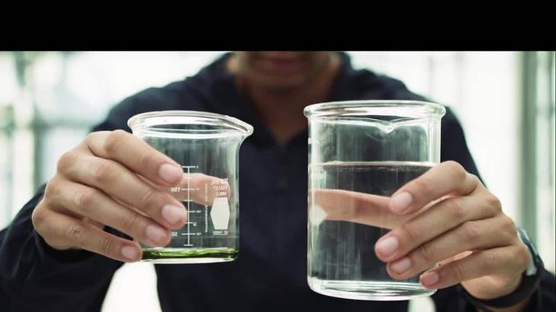 Hands holding two glass containers of water, demonstrating preparation of Grotek nutrients.